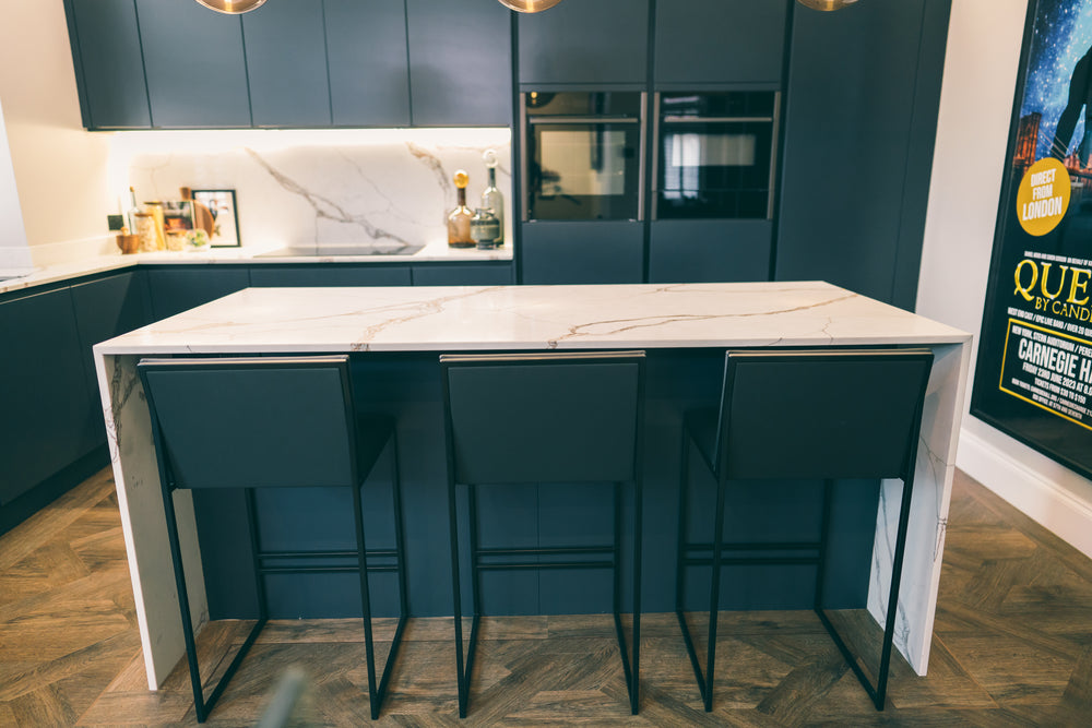 White porcelain waterfall island with black bar stools in front of navy tall units and built-in ovens
