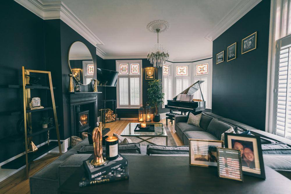 Cast-iron fireplace with a wood burner, brass ladder shelving and a grand piano in the bay of a period living room by Lisa Hensby Design & Build Studio.