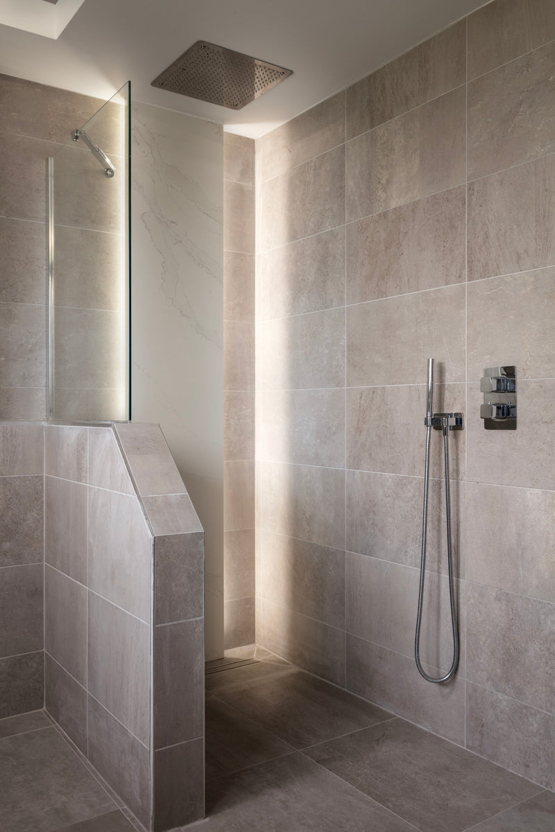 Walk-in shower with a ceiling rainfall head, glass screen and half-height tiled wall in warm grey tiles, in Lisa Hensby's own bathroom