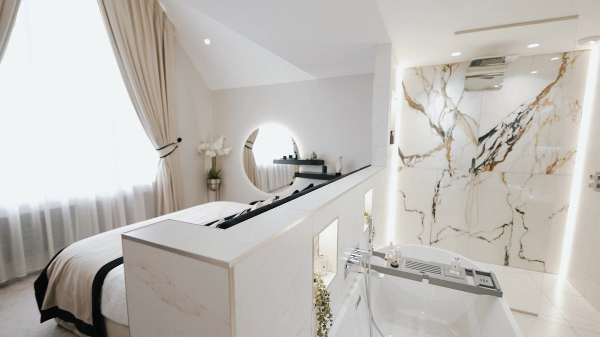 Bedroom by Lisa Hensby Design & Build Studio, with a half-height partition behind the bed opening onto a freestanding bath and a marble-effect shower.