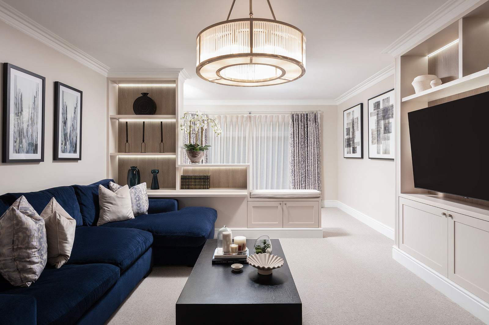 Living room in a Worsley home by Lisa Hensby Design & Build Studio, with a navy corner sofa, crystal drum chandelier and bespoke lit shelving around the TV.