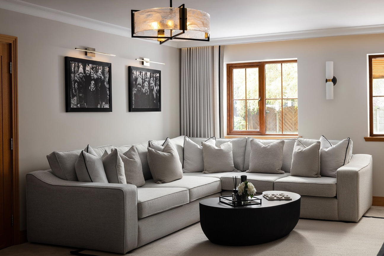 Neutral living room with oversized grey corner sofa, black oval coffee table, marble effect pendant light, brass wall lights and full length curtains — Lisa Hensby Design & Build Studio, Yorkshire