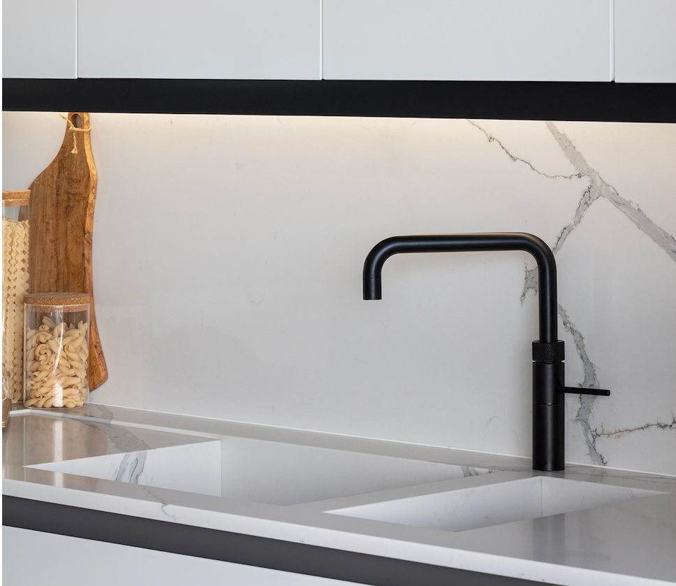 Modern kitchen design featuring a matte black mixer tap, marble worktop and splashback, and white handle-free cabinetry.