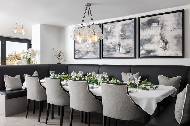 An elegant monochrome dining room featuring a curved black leather banquette, grey upholstered dining chairs, a statement bubble glass chandelier and a pair of large abstract artworks in muted greys and cream — designed by Lisa Hensby Design & Build Studio.