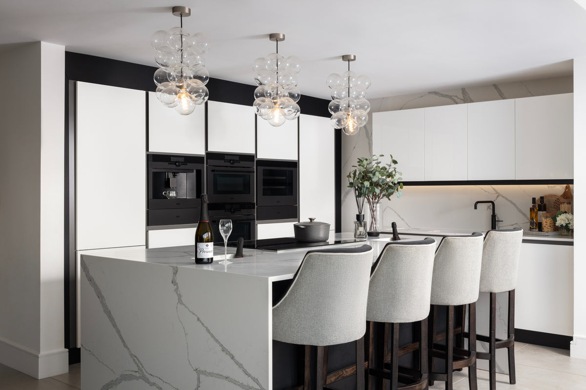 A stunning open-plan kitchen featuring a dramatic Calacatta marble waterfall island, handleless white cabinetry with black steel detailing, integrated appliances and a cluster of statement bubble glass pendant lights. Designed by Lisa Hensby Design & Build Studio.