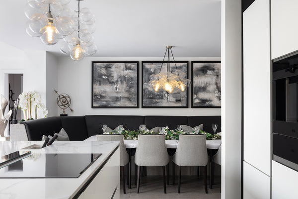Kitchen-diner from the quartz island and hob through to the dining booth, with charcoal banquette, grey chairs, glass bubble pendants and abstract canvases. Designed by Lisa Hensby Design & Build Studio.