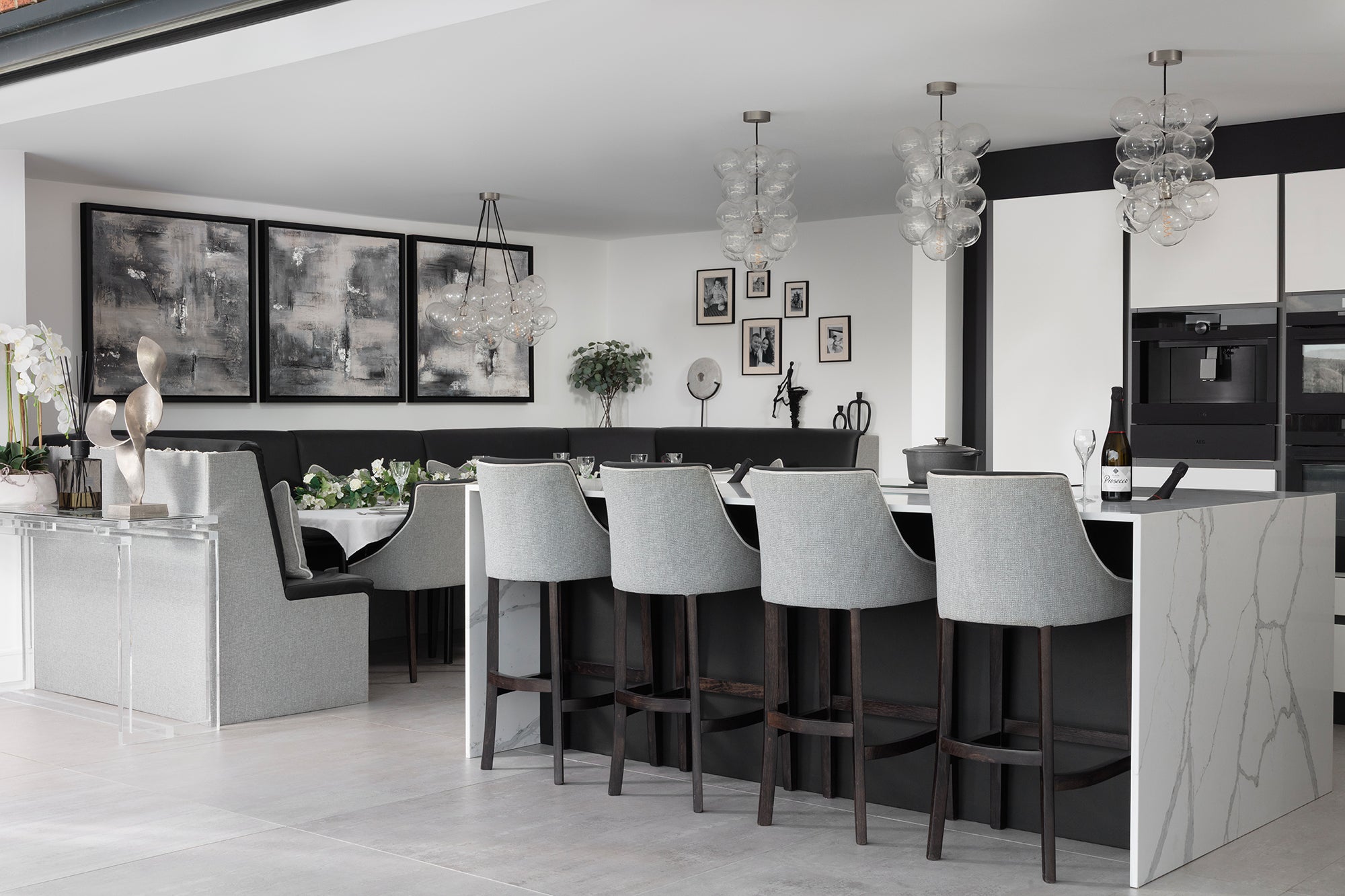 Open-plan kitchen-diner with the quartz island and grey bar stools, the corner dining booth beyond, glass bubble pendants and abstract canvases throughout. Designed by Lisa Hensby Design & Build Studio.