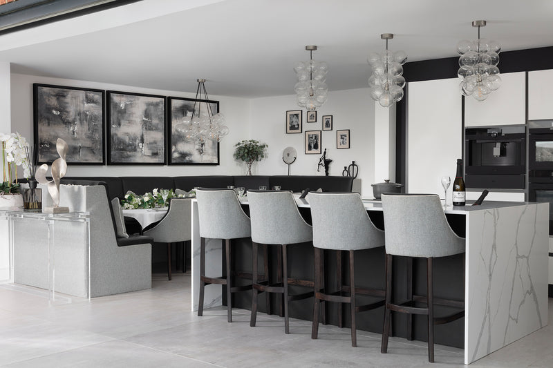 Open-plan kitchen-diner with the quartz island and grey bar stools, the corner dining booth beyond, glass bubble pendants and abstract canvases throughout. Designed by Lisa Hensby Design & Build Studio.