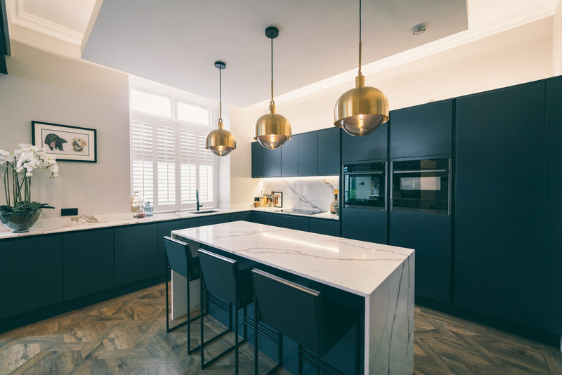 Navy handleless kitchen with a white porcelain waterfall island, brass globe pendants and herringbone wood floor
