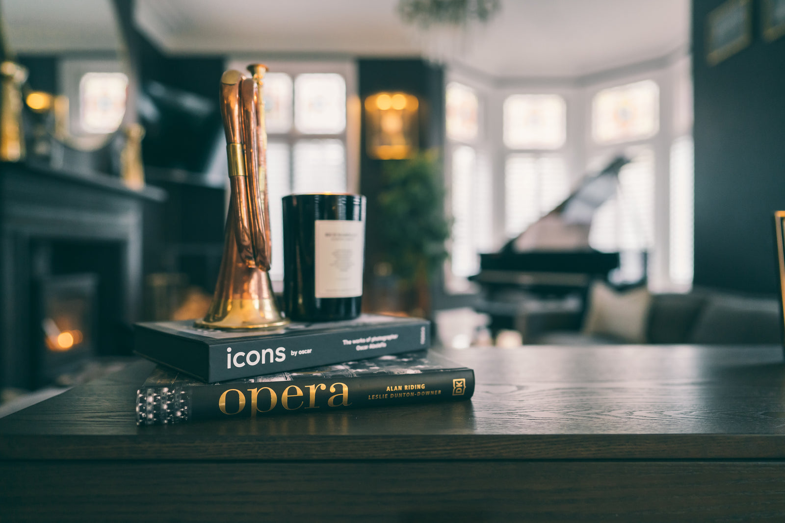 Styling detail of a copper sculpture, candle and books on a dark sideboard, with the grand piano softly blurred behind.