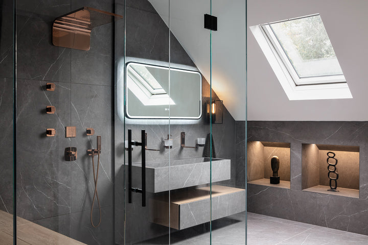 A luxury loft ensuite bathroom with dark grey marble-effect tiles, rose gold shower fittings, a wall-mounted stone basin, LED backlit mirror and Velux skylight - designed by Lisa Hensby Design & Build Studio.