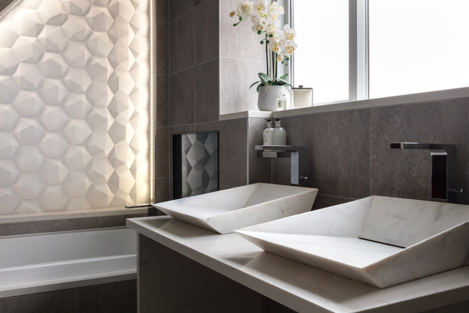 Twin angular white basins on a floating vanity beneath the window, beside a backlit 3D tile wall, in Lisa Hensby's own bathroom
