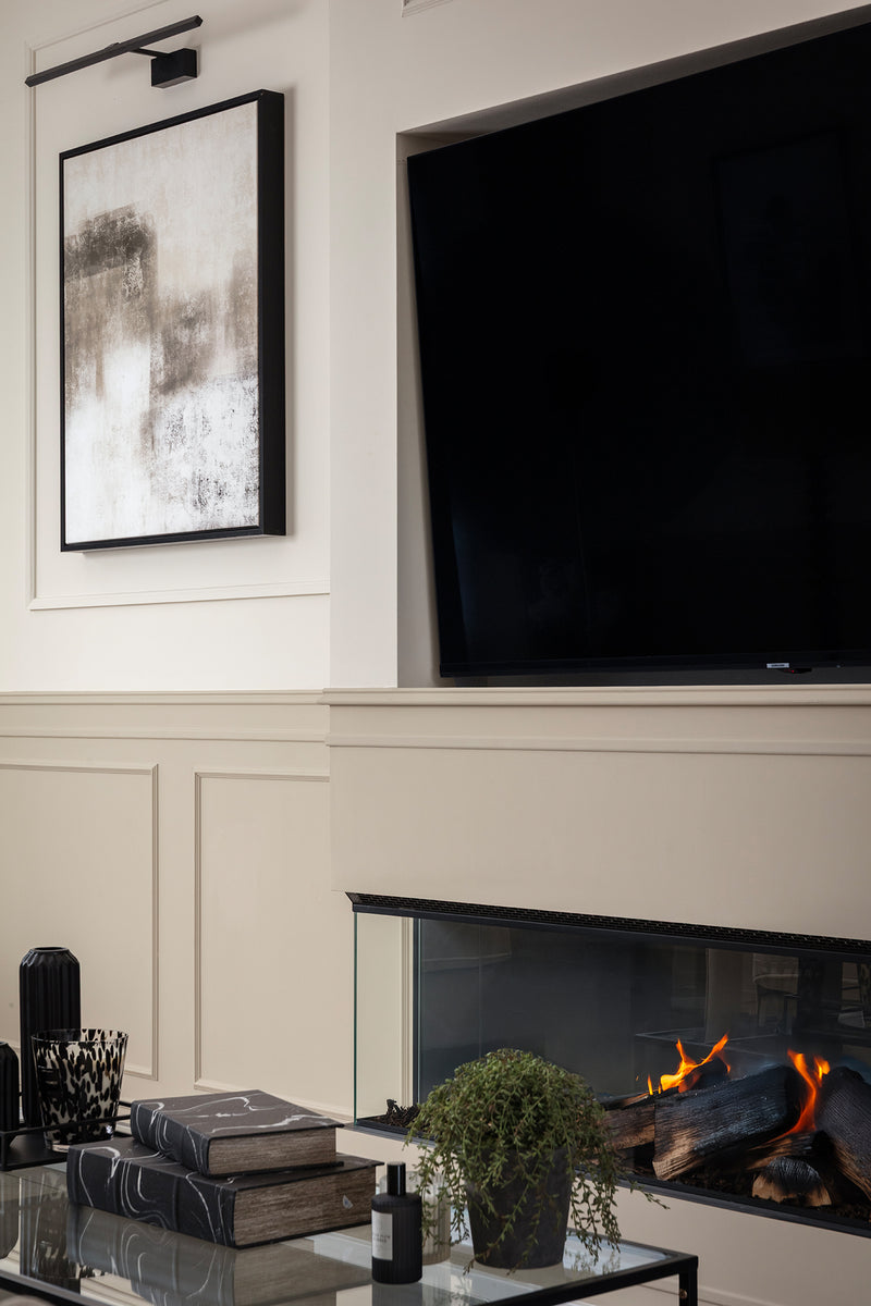 Living room feature wall with panelling painted in soft neutral, a wall-mounted TV, a glass-fronted fire with realistic logs and an abstract artwork in a slim black frame. Designed by Lisa Hensby Design & Build Studio.