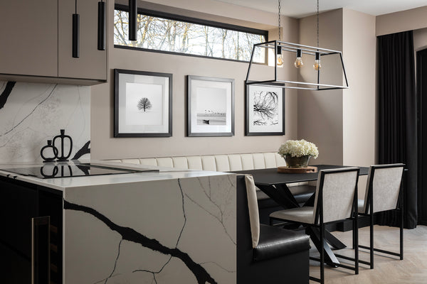 Dining booth with a cream banquette, black table and caged pendant light, set beside the quartz waterfall island beneath a high-level window. Designed by Lisa Hensby Design & Build Studio.