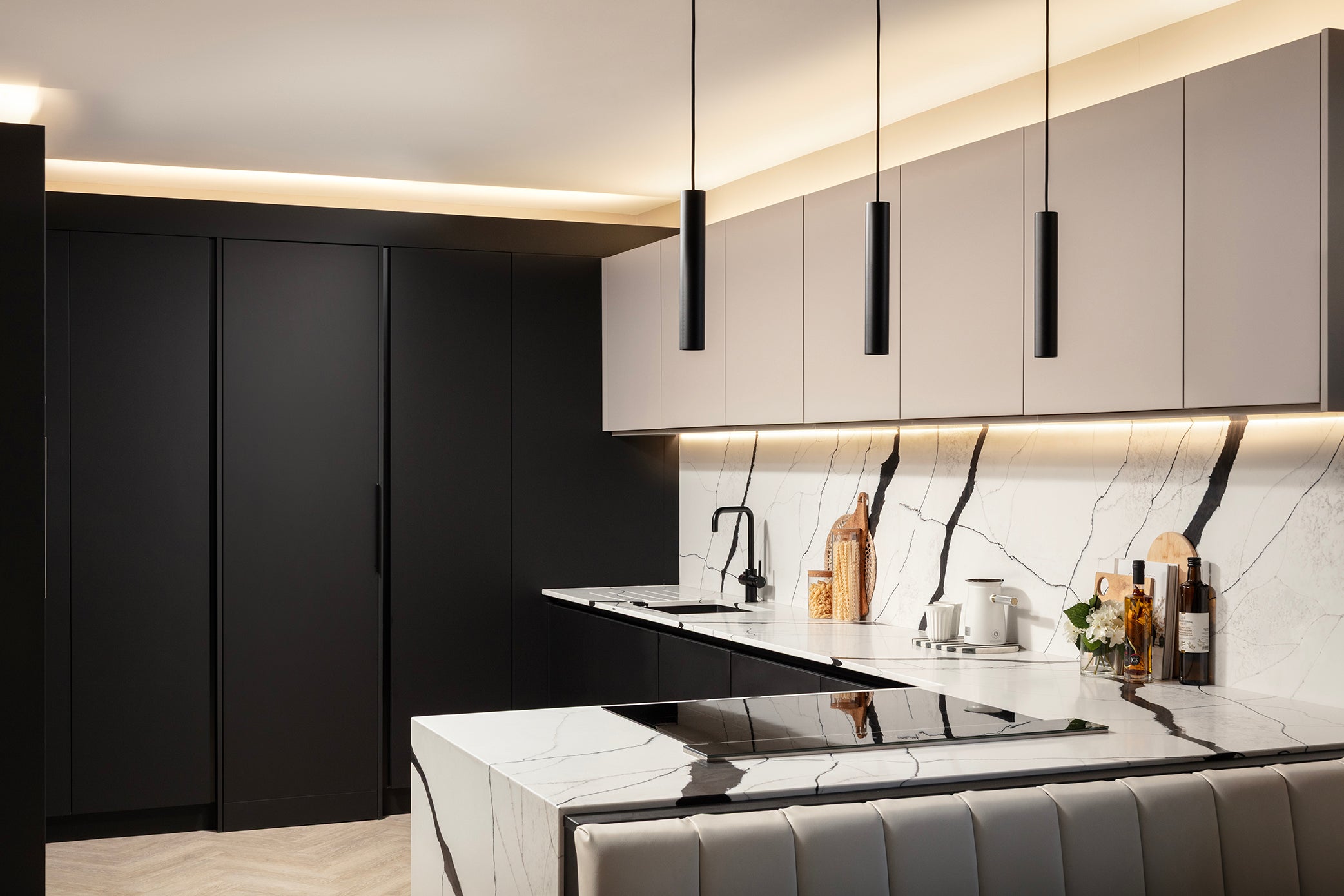 Floor-to-ceiling jet black units, including the concealed utility room door, beside cashmere wall units, the marble-effect splashback and the quartz waterfall island. Designed by Lisa Hensby Design & Build Studio.