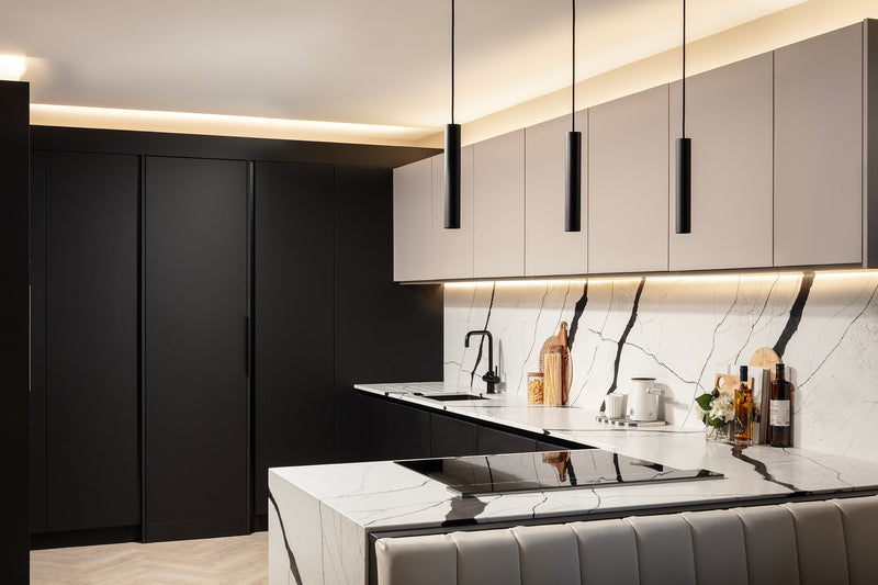 Floor-to-ceiling jet black units, including the concealed utility room door, beside cashmere wall units, the marble-effect splashback and the quartz waterfall island. Designed by Lisa Hensby Design & Build Studio.