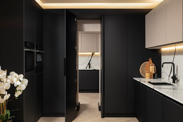 A concealed jet black cabinet door opens to reveal the hidden utility room behind, with the main kitchen run and integrated ovens alongside. Designed by Lisa Hensby Design & Build Stuio.
