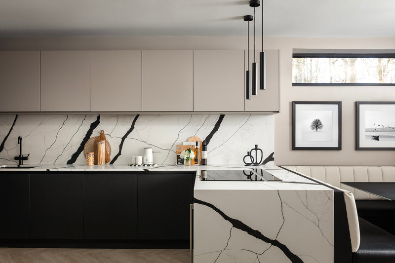 Kitchen-diner with cashmere wall units, jet black base units and a quartz waterfall island, alongside a banquette booth beneath a new window. Designed by Lisa Hensby Design & Build Studio.