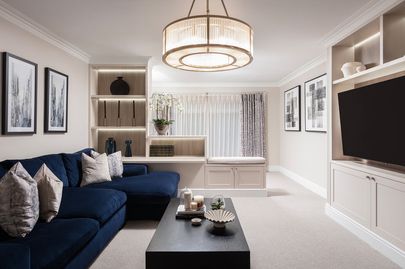 Living room in a Worsley home by Lisa Hensby Design & Build Studio, with a navy corner sofa, crystal drum chandelier and bespoke lit shelving around the TV.
