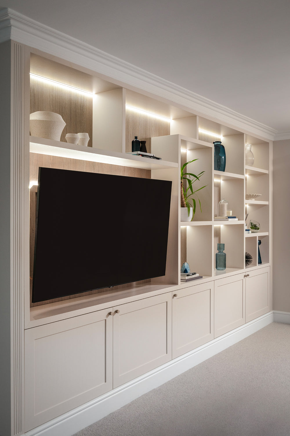 Floor-to-ceiling bespoke media wall with lit open shelving and cupboards below, designed by Lisa Hensby Design & Build Studio.
