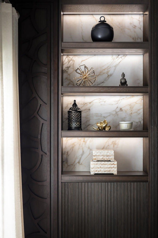 Dark wood built-in shelving with a marble backing and integrated lighting, styled with black, gold and ivory decorative pieces. Designed by Lisa Hensby of Lisa Hensby Design & Build Studio.