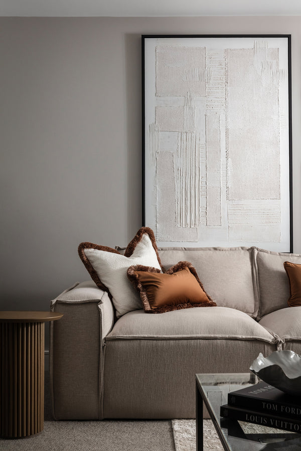 Cosy living room corner with a beige sofa, rust-brown cushions, a textured white abstract canvas and a fluted wood side table. Designed by Lisa Hensby of Lisa Hensby Design & Build Studio.