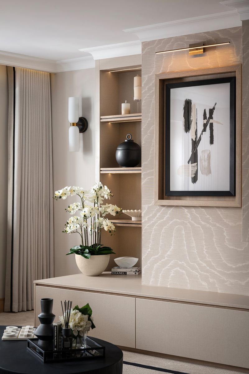 Media wall detail with illuminated niches, marble-effect porcelain, a walnut-framed abstract print and white orchid, styled with candles and decorative objects in warm neutral tones. Designed by Lisa Hensby Design & Build Studio.