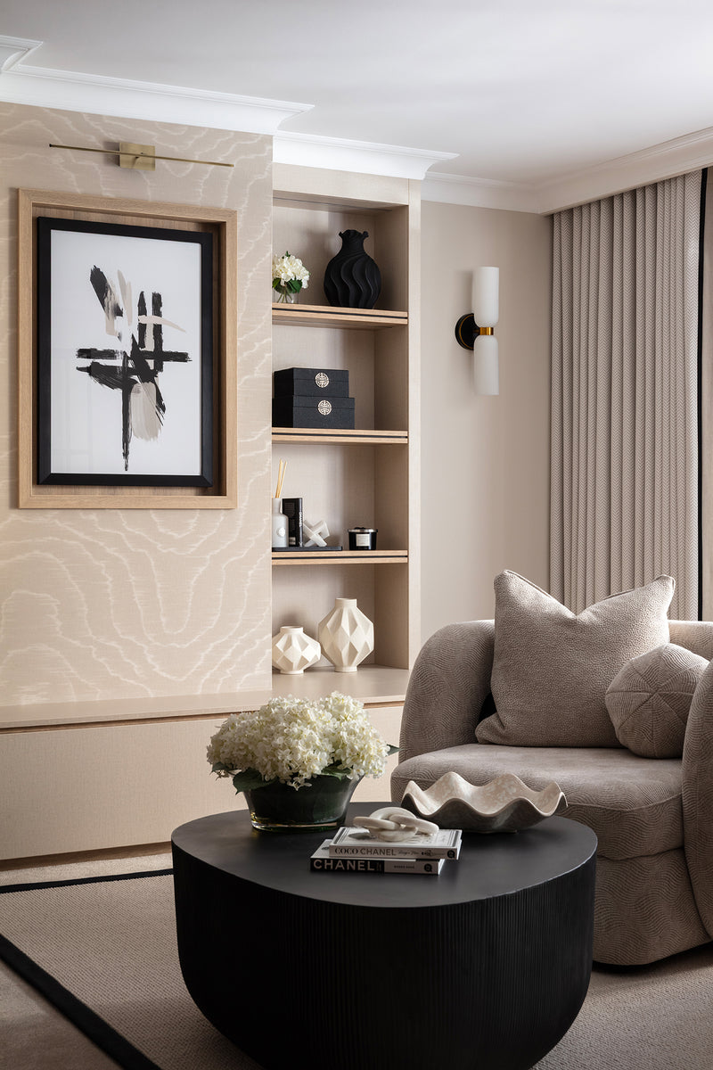 Screen-free reading corner with a sculptural cream armchair, a round black coffee table and built-in shelving displaying a framed abstract print, candles and decorative objects. Designed by Lisa Hensby of Lisa Hensby Design & Build Studio