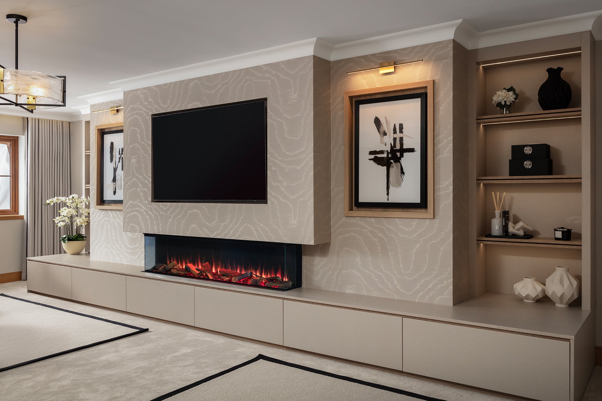 Floor-to-ceiling media wall with a wall-mounted TV, a linear log-effect fire and marble-effect porcelain, flanked by illuminated built-in shelving and framed abstract artwork. Lisa Hensby Design & Build Studio.