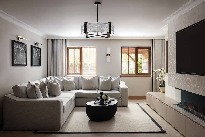 Boutique-hotel-inspired living room with a large neutral corner sofa, round black coffee table, sculptural glass pendant and a media wall with a wall-mounted TV and linear fire. Designed by Lisa Hensby Design & Build Studio.